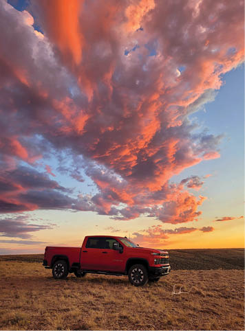 A red pickup truck is parked in a field with a beautiful sunset in the background. AI generated content